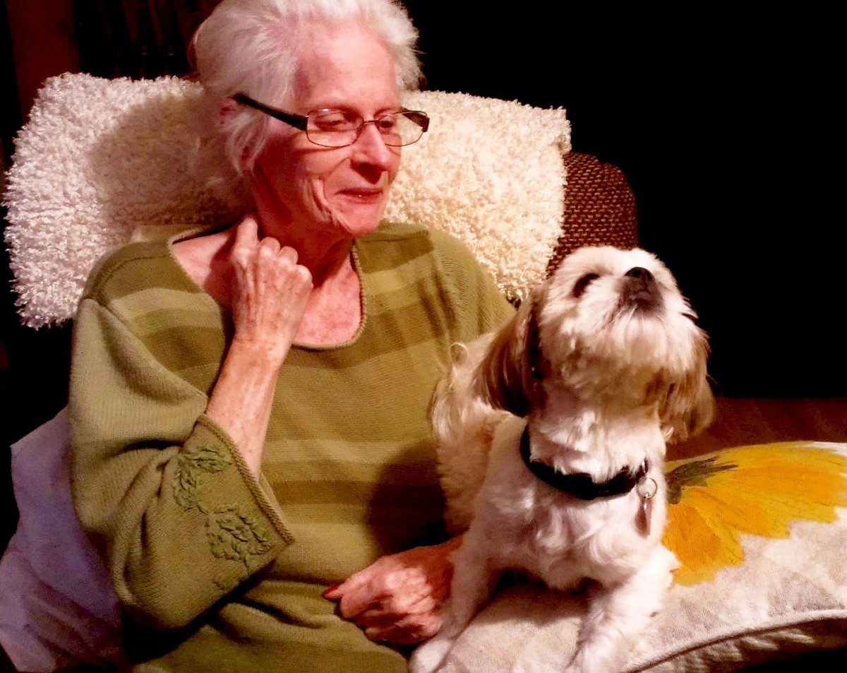 An elderly woman sitting with her dog on a couch indoors.