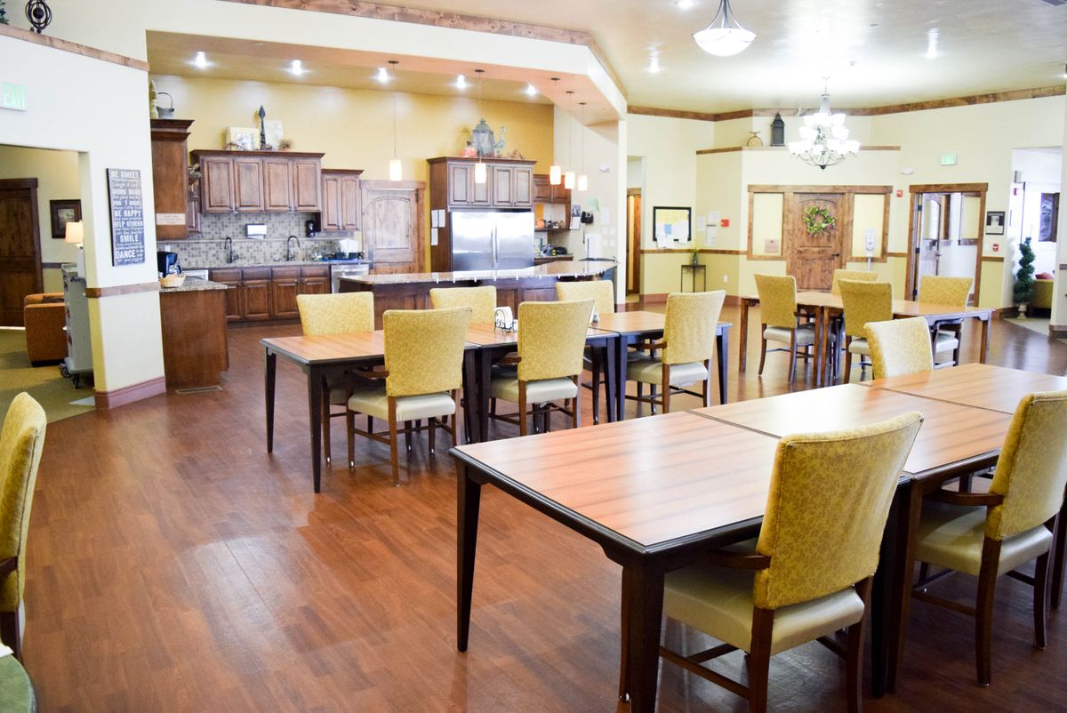 A spacious and well-lit dining area with wooden tables and chairs, connected to a kitchen space.