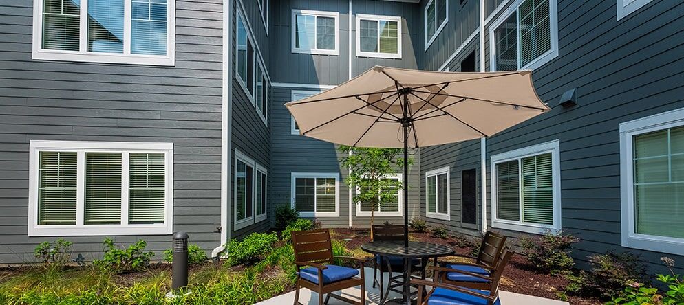 A cozy patio area with an umbrella, chairs, and a table set against a residential building.