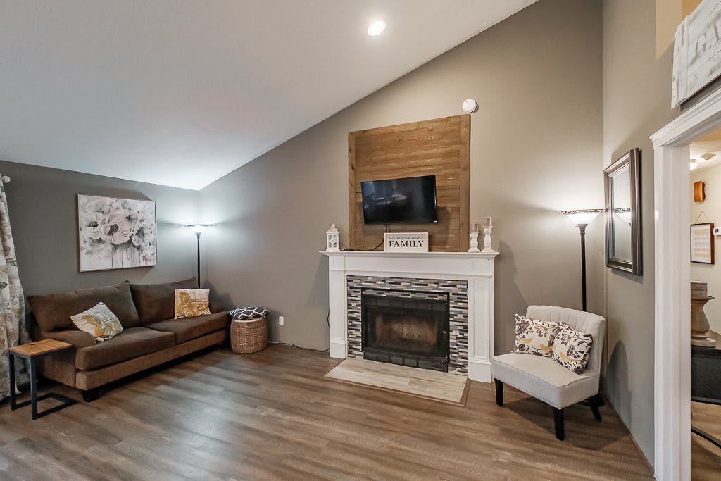 A cozy living room with a fireplace, sofa, and television, featuring modern decor and wood flooring.