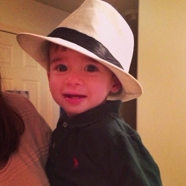 A young child wearing a fedora and smiling indoors.