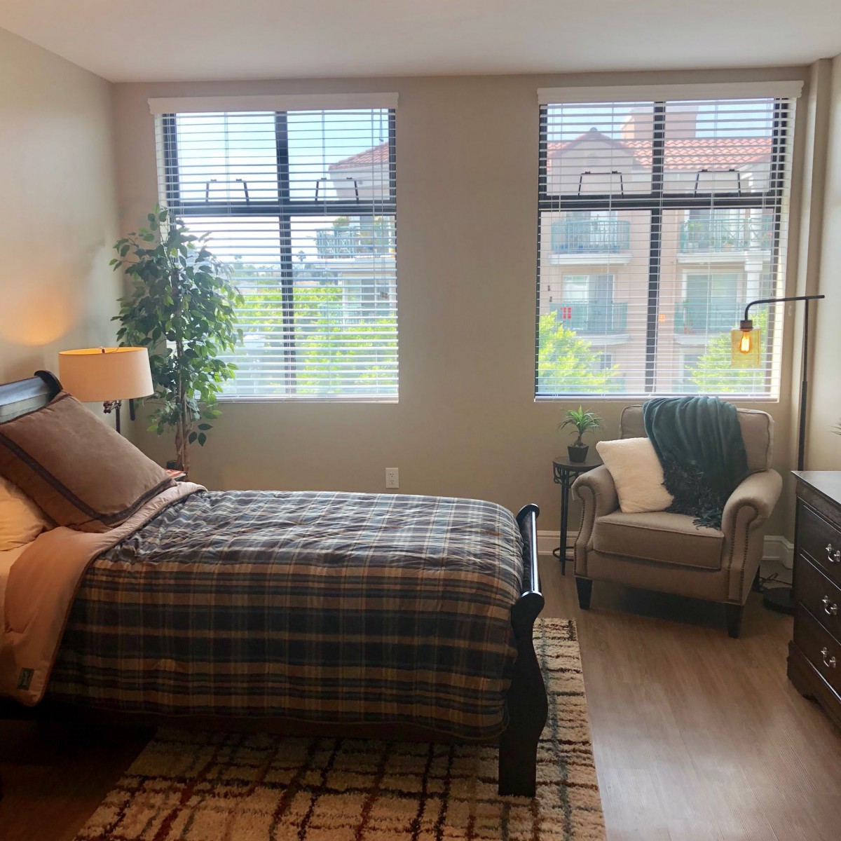 A cozy bedroom with a plaid bedspread, large windows, and comfortable seating.