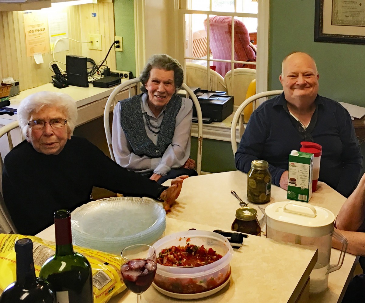A group of three people sitting at a table with food and drink items in a cozy kitchen setting.