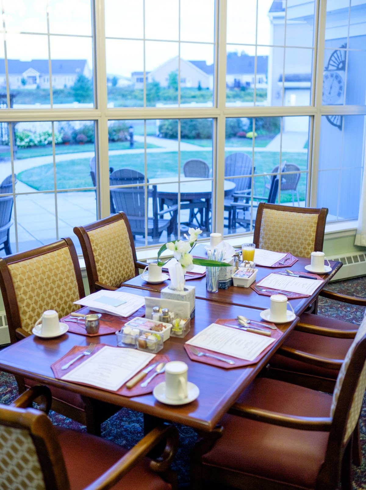 A well-set dining table with chairs by a large window offering a view of the outdoor patio.
