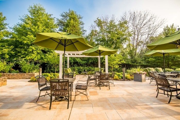 A peaceful outdoor patio area with tables, chairs, and green umbrellas surrounded by lush trees.