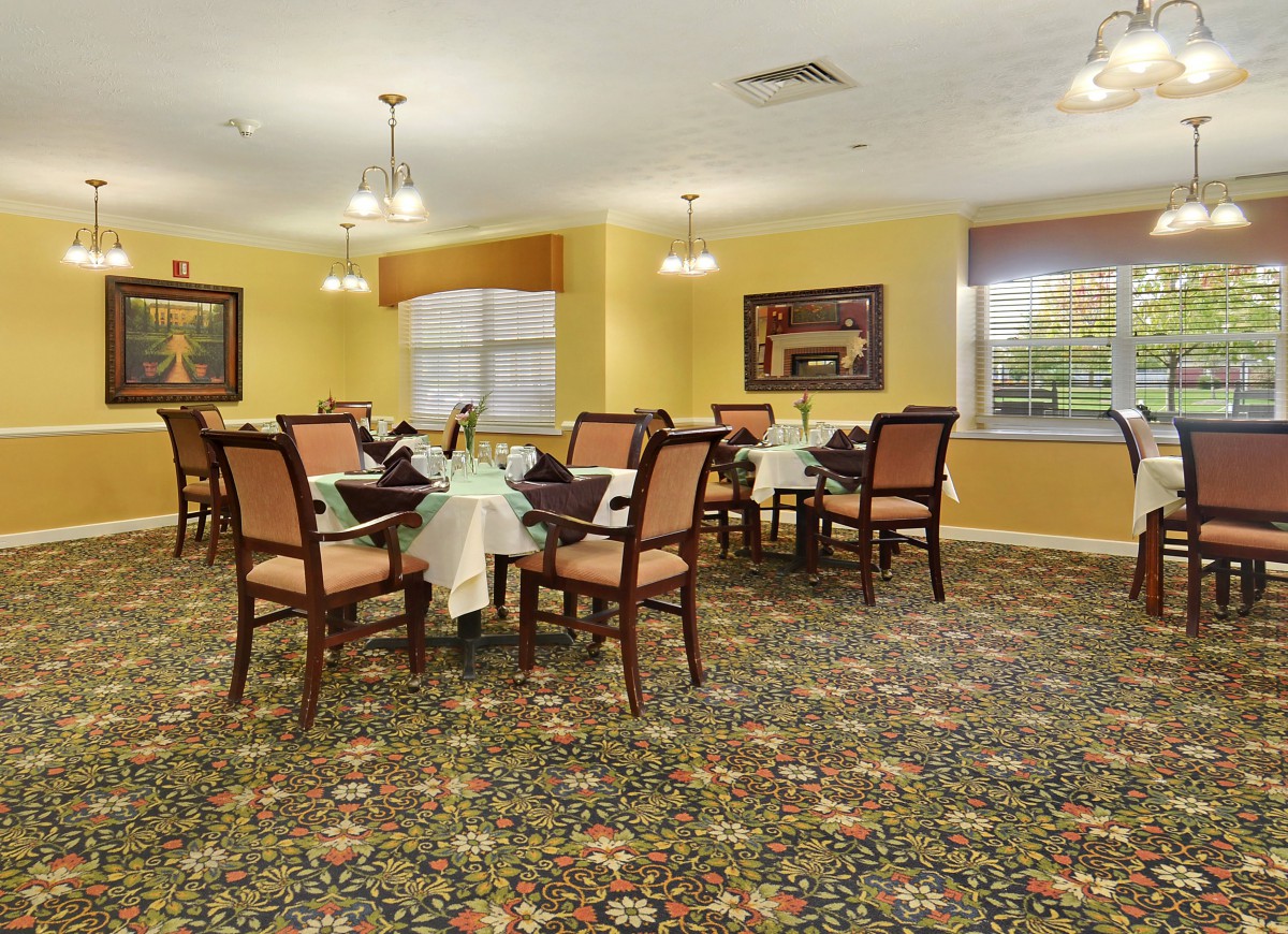 A well-appointed dining room with neatly arranged tables and chairs, featuring elegant lighting and patterned carpet.