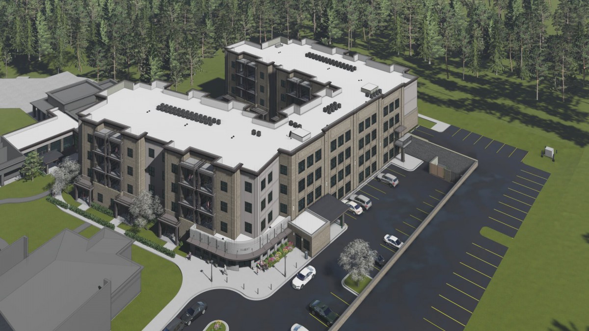 A bird's-eye view of a modern multi-story building surrounded by a forest with an adjacent parking lot.