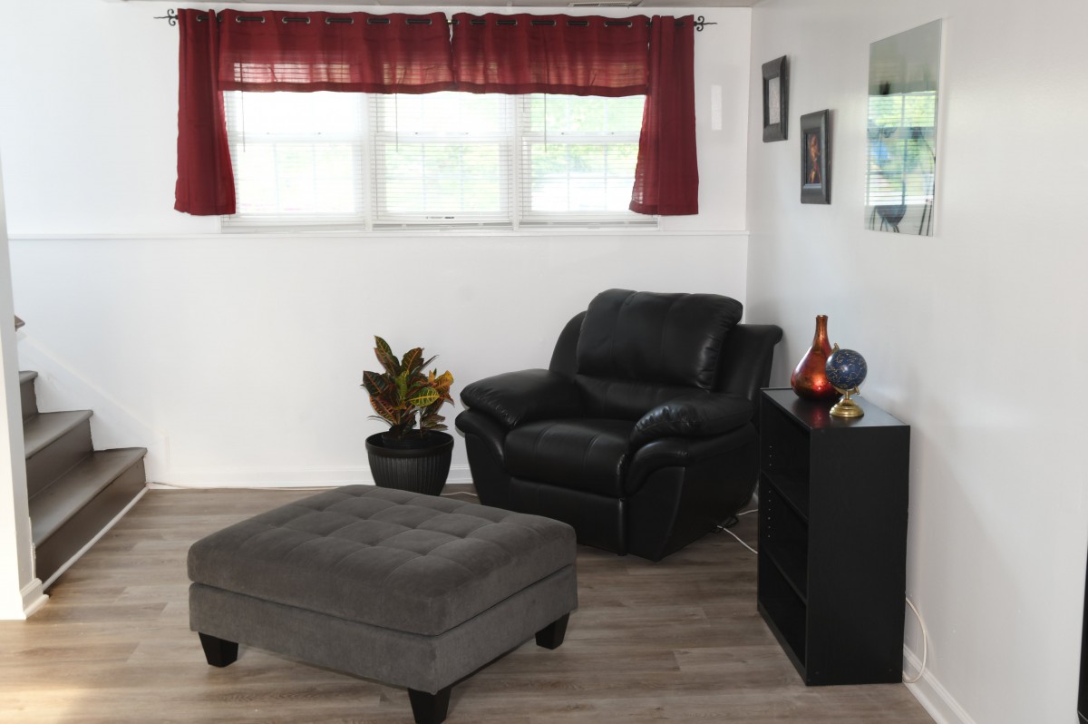 A cozy living room corner with a black chair and ottoman, accented by a potted plant and decorative items.