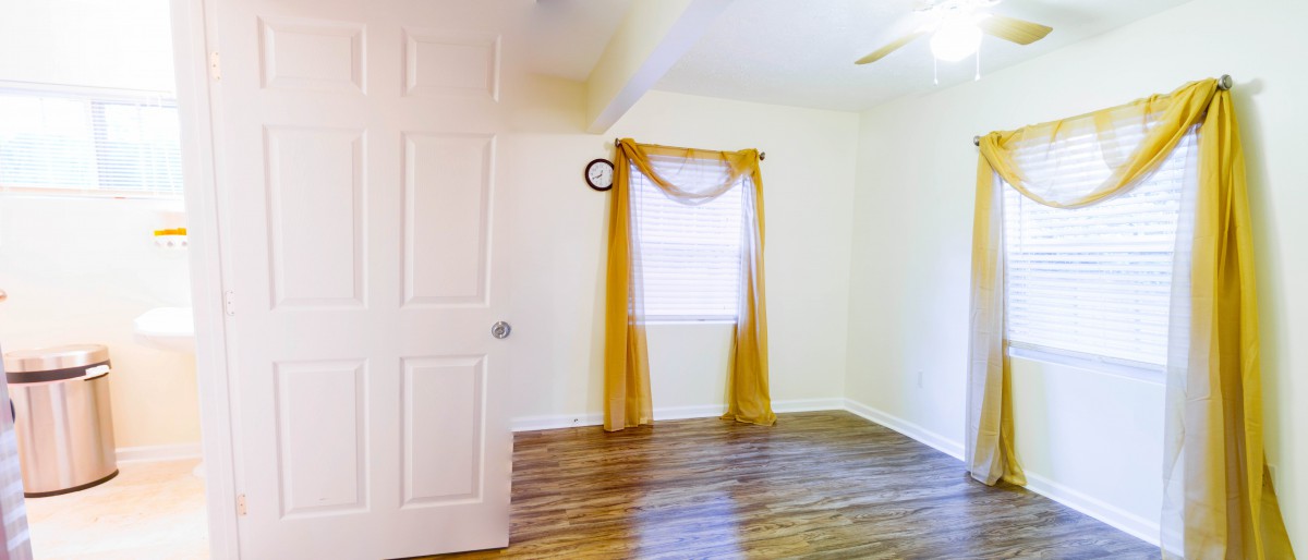 An empty room with hardwood flooring and yellow curtains.