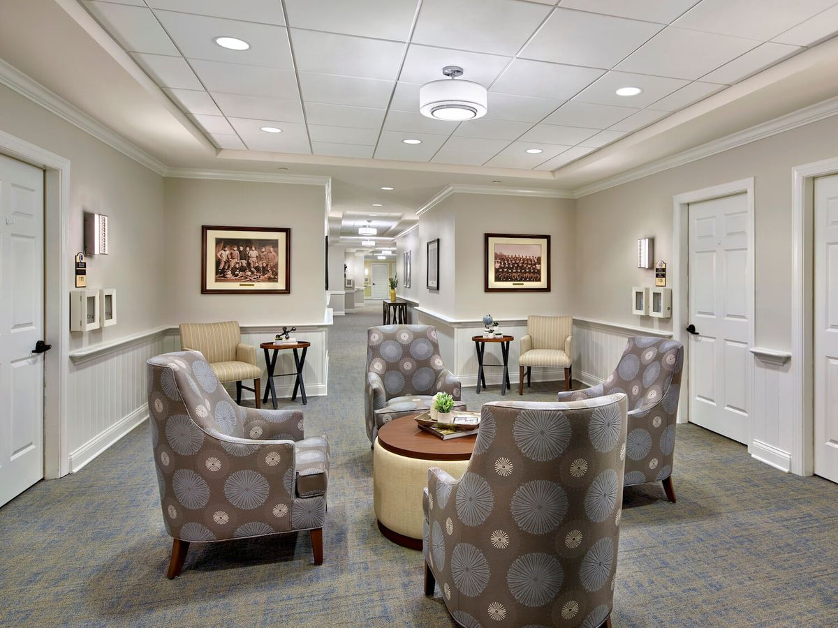 A modern lobby featuring a cozy seating area with patterned chairs and a central table, leading to a hallway.