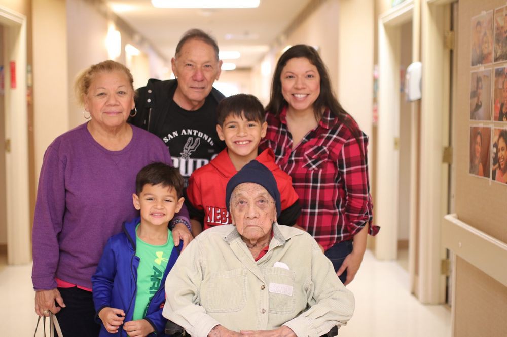 A family posing with an elderly man in a wheelchair inside a hallway.