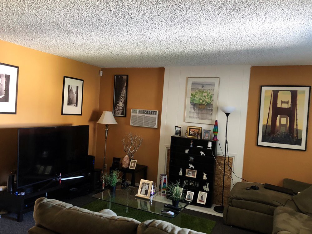 A cozy living room with artwork on orange accent walls, featuring a large TV, sofas, and decorative shelves.