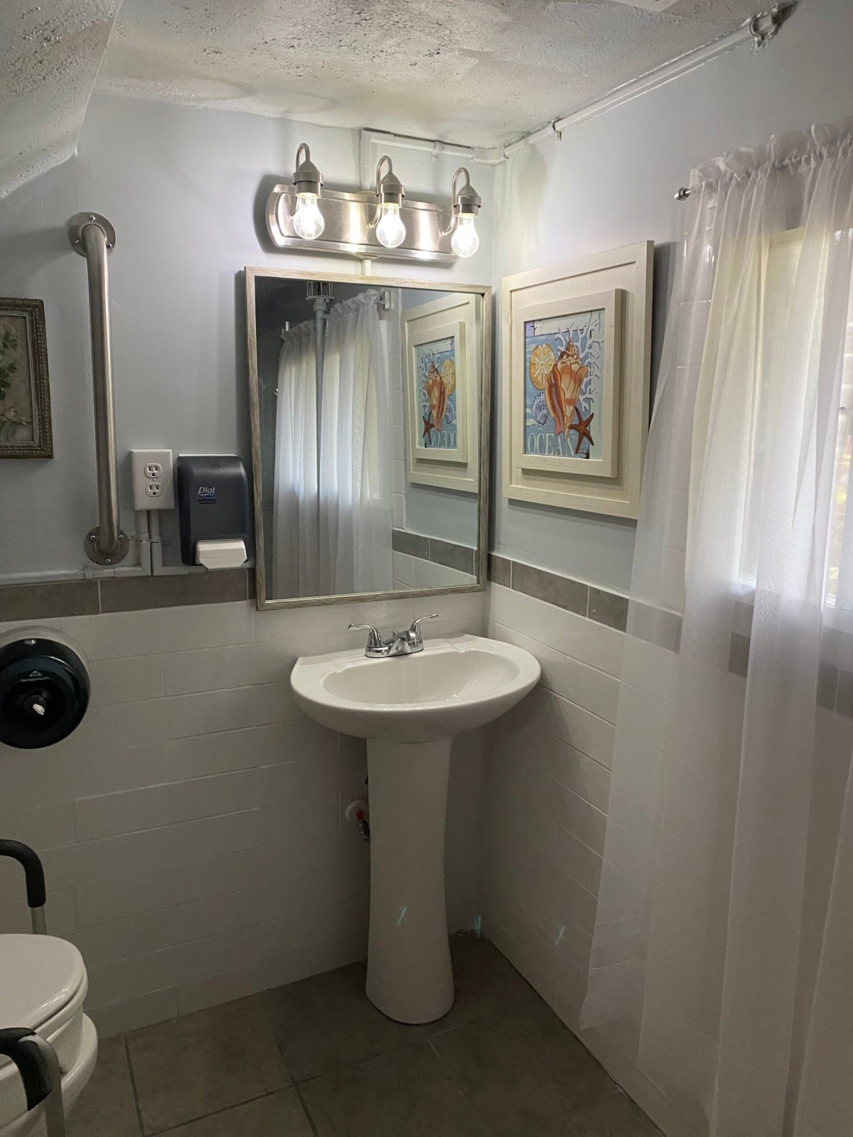 A clean, well-lit bathroom with a pedestal sink and framed artwork on the walls.