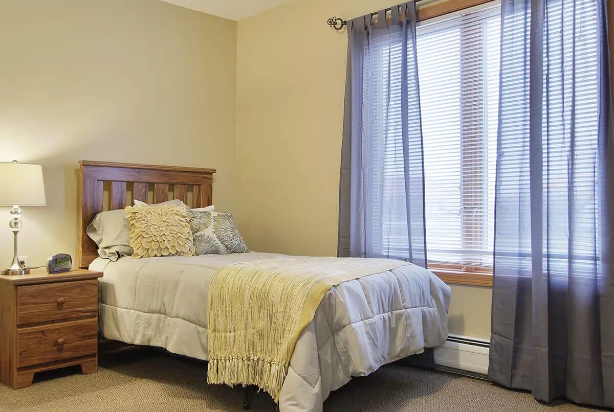 A cozy bedroom with a bed adorned with pillows and a throw, featuring a window with curtains.