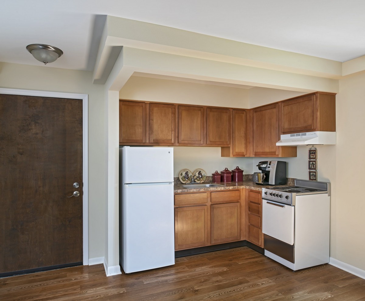 A modern apartment kitchen with wooden cabinets and standard appliances.