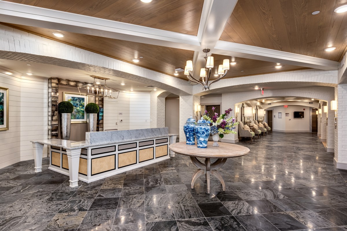An elegant hotel lobby with a chandelier, reception desk, and marble flooring.
