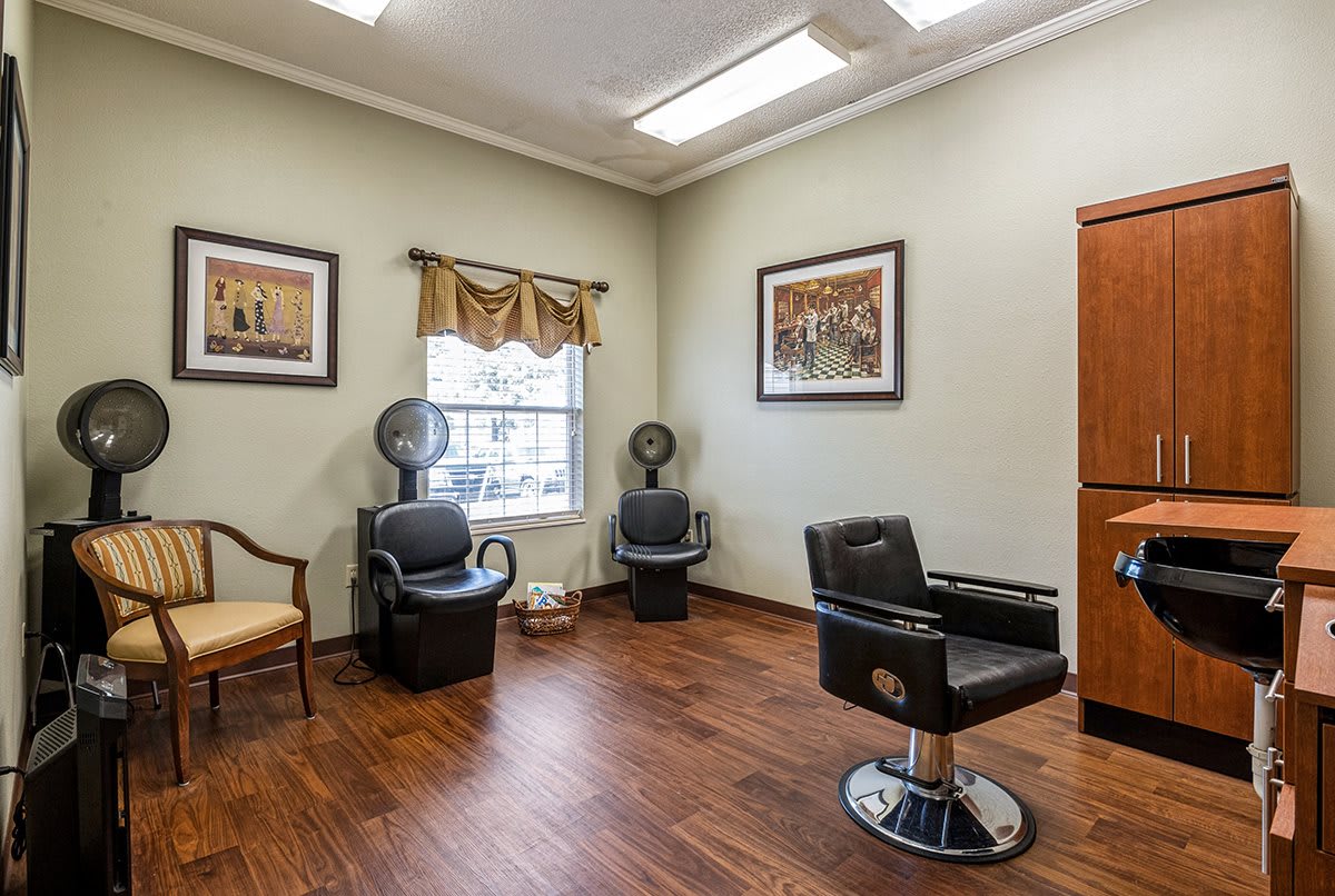 A well-lit salon with a barber chair and hairdryer chairs, featuring wood flooring and wall art.