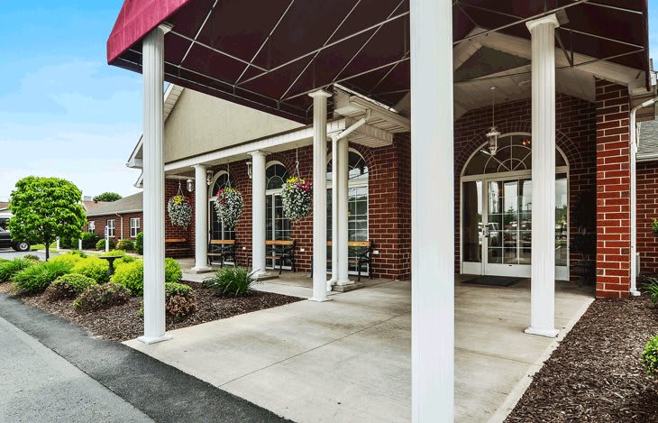 The entrance of a brick building with white columns and a red awning.