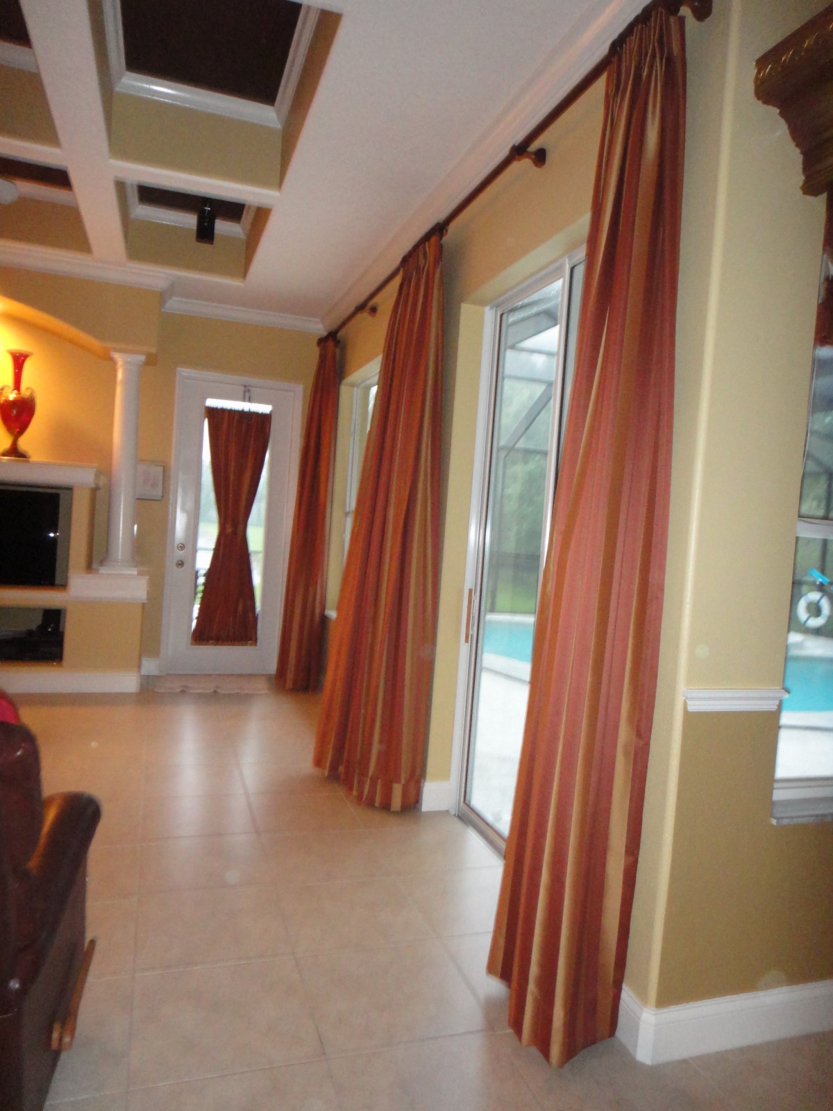A modern living room with large windows overlooking a pool, featuring elegant curtains and stylish decor.