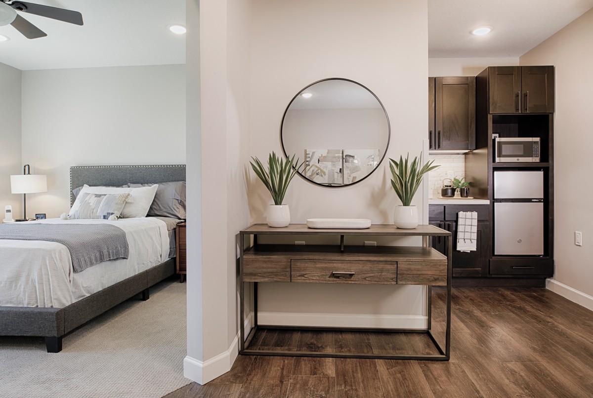 A contemporary bedroom features a stylish console table with plants and a round mirror, complemented by wood flooring.