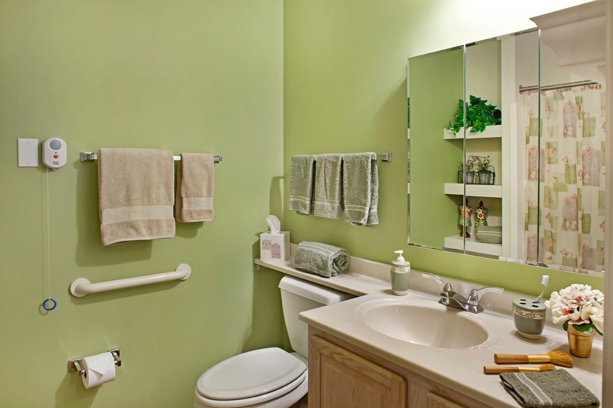 A bathroom with green walls featuring a sink, toilet, mirror, and shelves.