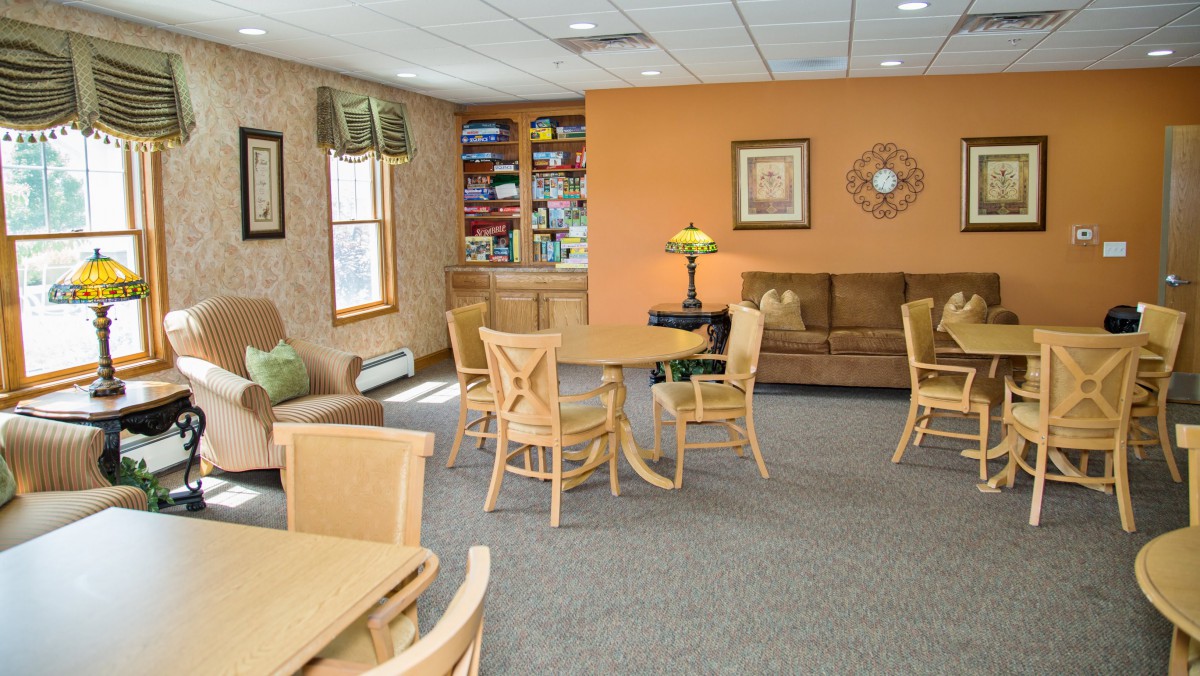A cozy living room featuring a sofa, several chairs around tables, and a bookshelf in the background.