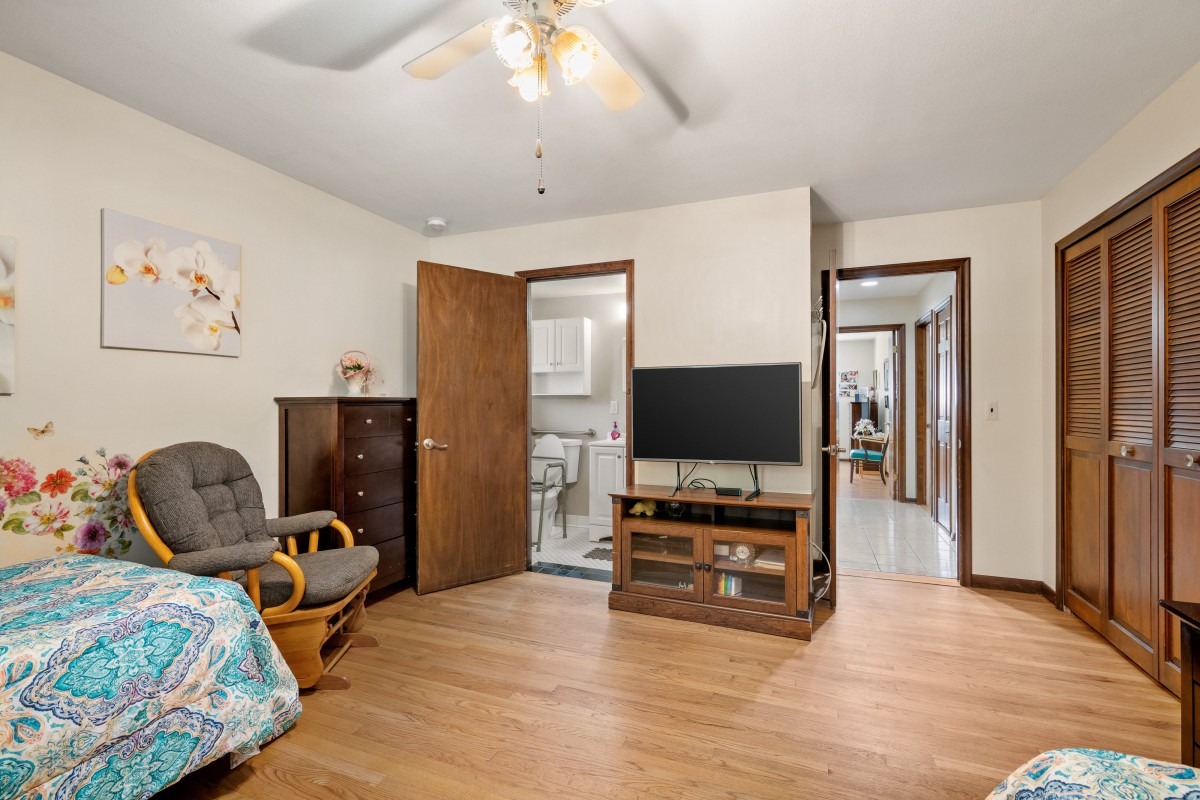 A cozy living room with a television, ceiling fan, and wooden flooring.