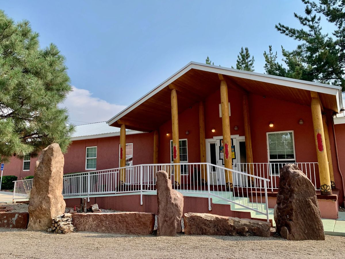 A modern building with a ramp entrance, surrounded by trees and large stones.