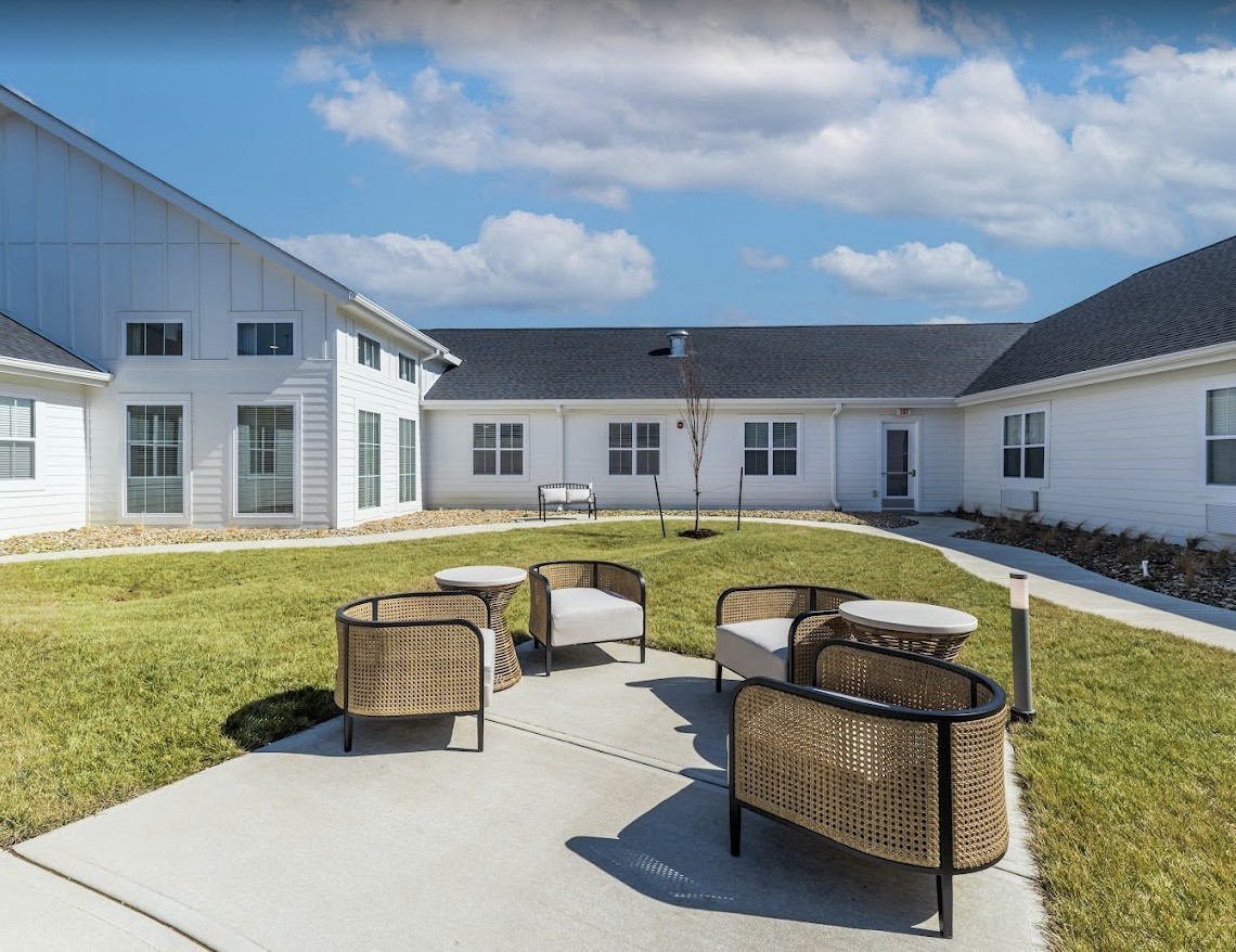 A courtyard with outdoor seating and a modern building in the background under a partly cloudy sky.