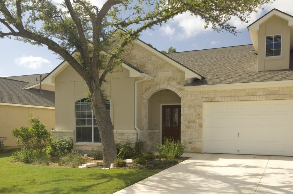 A suburban house with a tree in the front yard and a spacious driveway.