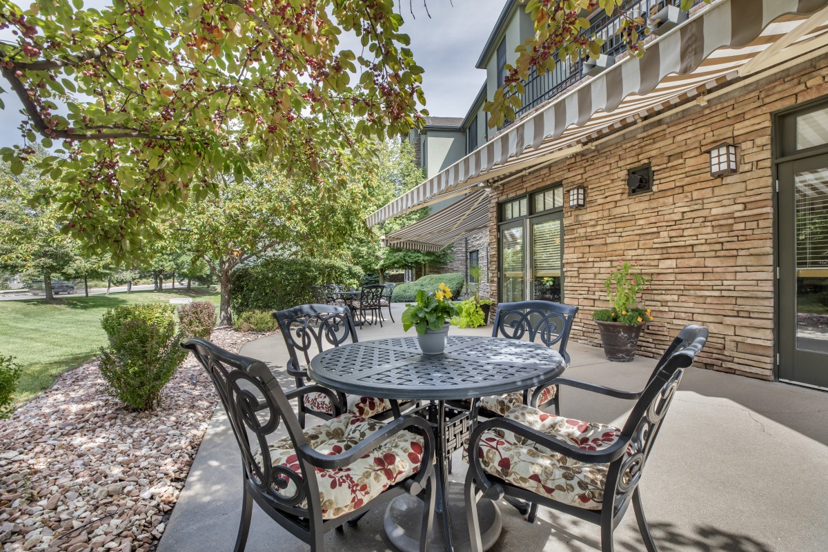 A cozy outdoor patio with a table and cushioned chairs surrounded by lush greenery.