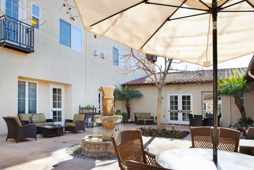 A serene outdoor patio with a central fountain, surrounded by chairs and shaded by umbrellas.