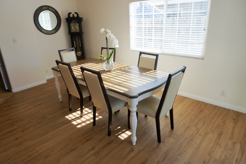 A modern dining room with a wooden table and six chairs, illuminated by natural light from a window.