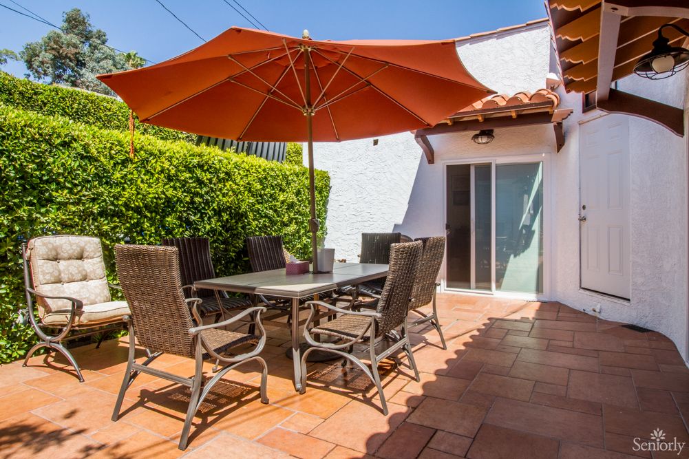A sunny patio with outdoor furniture, featuring a large orange umbrella and terracotta tiles.