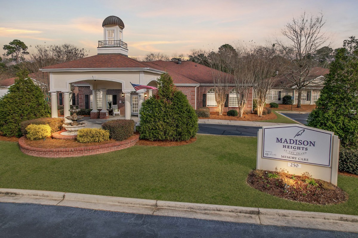 A charming building entrance with a welcoming sign, surrounded by manicured landscaping at twilight.