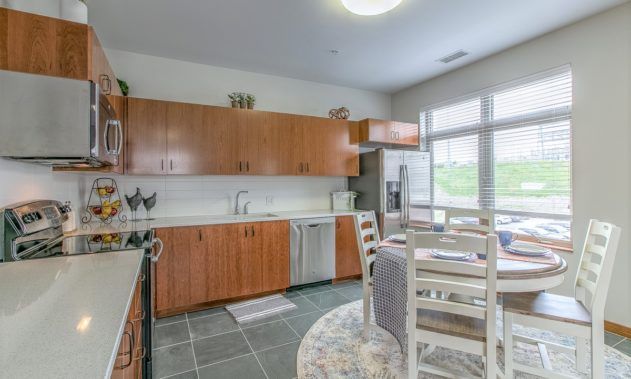 A modern kitchen with wood cabinets and a dining area, illuminated by natural light.
