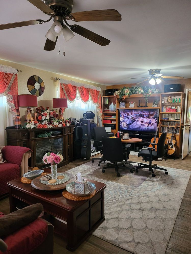 A cozy living room with a home office setup, featuring a television, bookshelves, and musical instruments.
