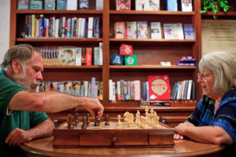 Two people playing chess in front of a bookshelf.