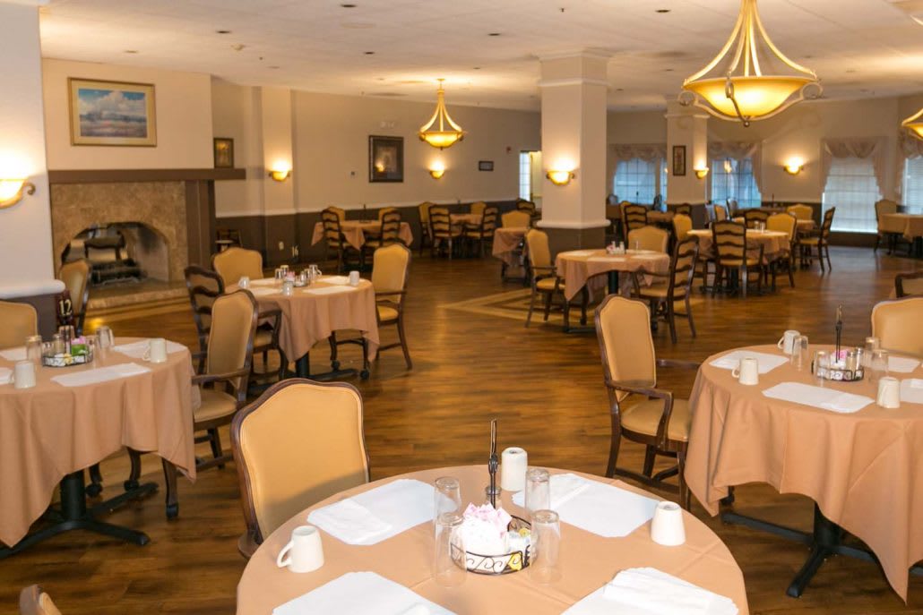 An elegant restaurant dining room with neatly arranged tables and chairs, featuring warm lighting from chandeliers.