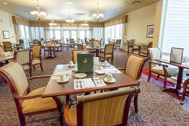A formal dining room with neatly arranged tables and chairs, featuring elegant chandeliers.