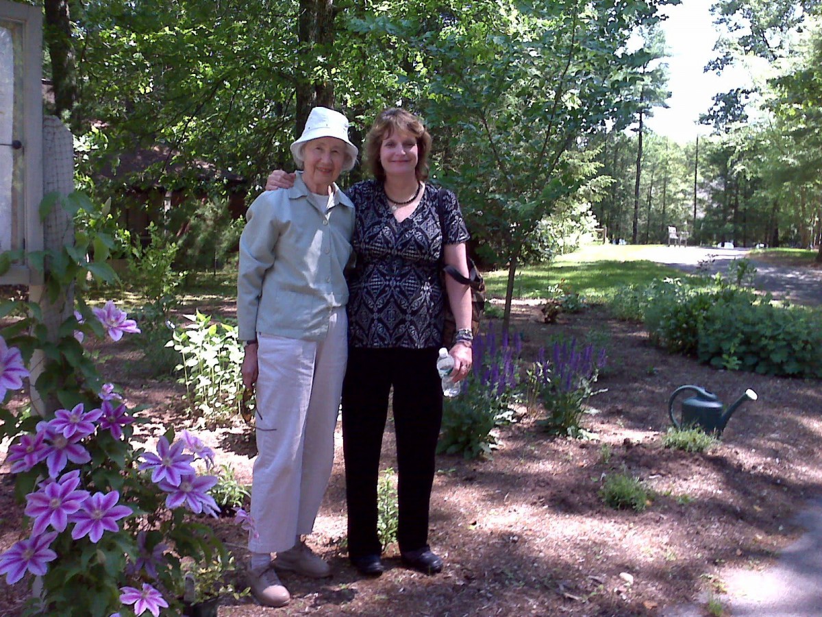 Two people standing together in a garden surrounded by greenery and flowers.