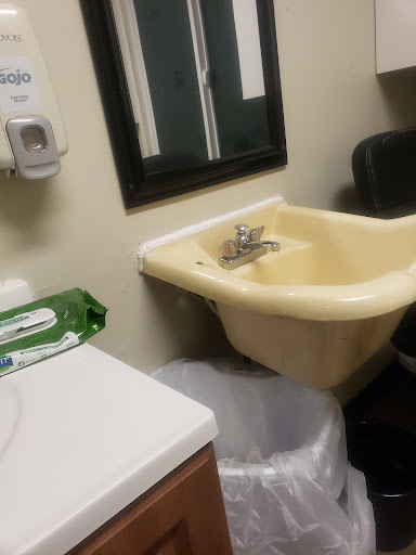 A small bathroom area featuring a yellow sink, a mirror, and a trash can.