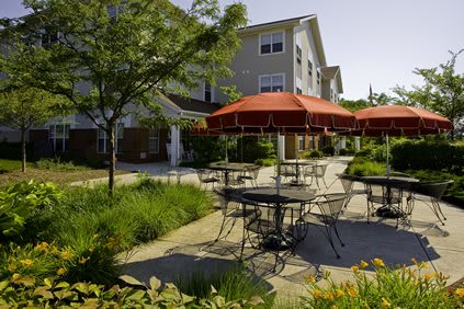 A tranquil residential patio with tables and red umbrellas surrounded by lush landscaping.