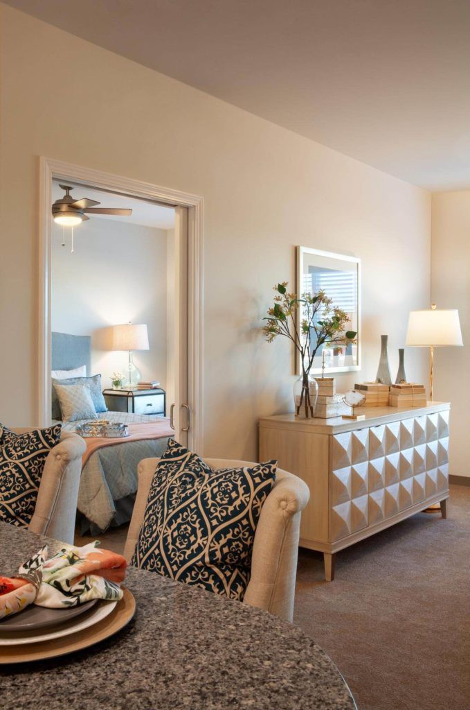 A cozy living room featuring stylish furniture and decor, with a view into a well-lit bedroom.