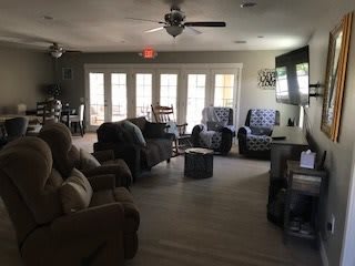A cozy living room with sofas, chairs, and a TV, illuminated by natural light from large windows.