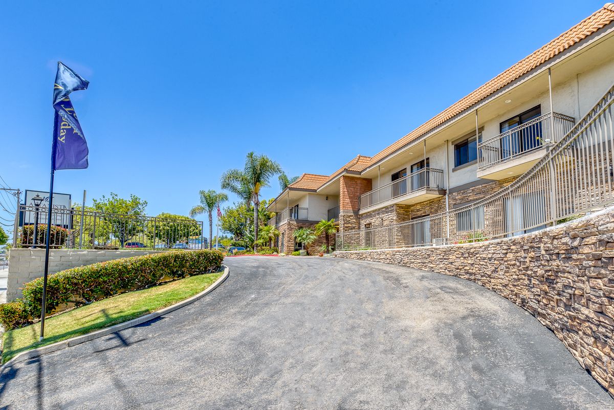 A sunny view of a building with a driveway lined by palm trees.
