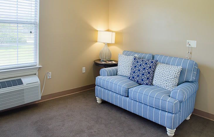 A cozy living room corner with a striped sofa, decorative cushions, and a warm lamp.