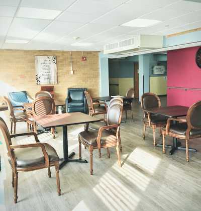 An empty cafe with wooden floors, tables, and chairs illuminated by daylight.