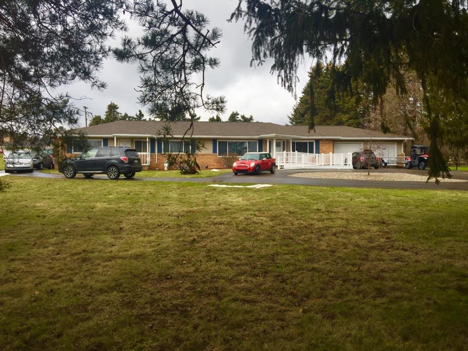 A residential house with several cars parked on the lawn under an overcast sky.