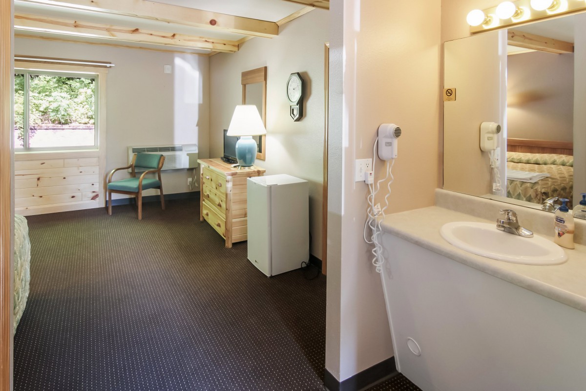 A cozy hotel room interior with a dresser, bedside lamp, and sink area.